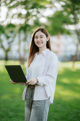Happy woman sits in park with laptop. Portrait of a young freelance woman working outdoors. Online, technology concept