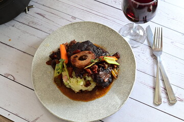 Plated serving of braised beef with bone in red wine sauce, accompanied by tender potatoes, root vegetables, and fresh herbs