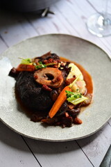 Plated serving of braised beef with bone in red wine sauce, accompanied by tender potatoes, root vegetables, and fresh herbs