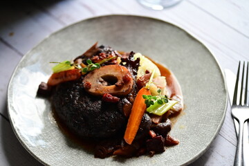 Plated serving of braised beef with bone in red wine sauce, accompanied by tender potatoes, root vegetables, and fresh herbs