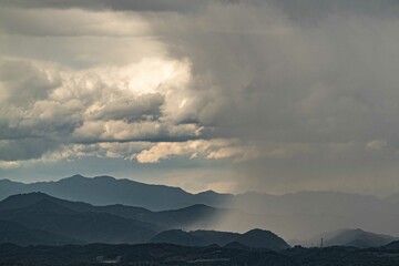 重い雨雲から山の向こうに雨柱で土砂降りが降り注ぐ