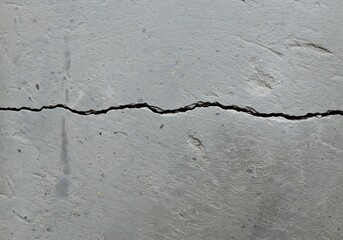 Obraz premium A rough light gray concrete surface is bisected by a prominent, jagged crack running horizontally, accompanied by minor branching fissures indicating stress.