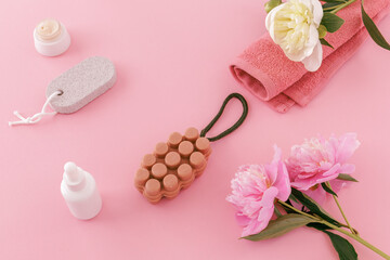 Towel with body care products and peony flowers on the pink background.