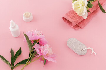Towel with body care products and peony flowers on the pink background.