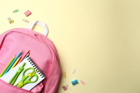 Pink backpack with colorful stationery items on a beige yellow background, top view