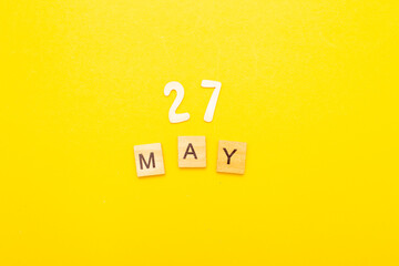 Top view of word 27 May calendar date made by wooden cubes on yellow color background