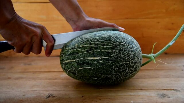The man use knife split the orange melon on wood plate