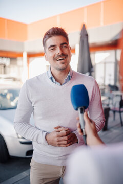 Smiling businessman giving interview to journalist with microphone outdoors