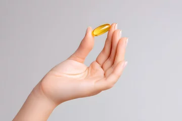 Zelfklevend Fotobehang Close-up Woman's hand holding omega 3 fish oil capsule isolated on white background © Oksana