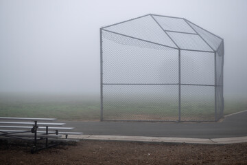 playground chain-link backstop and bleacher in thick fog