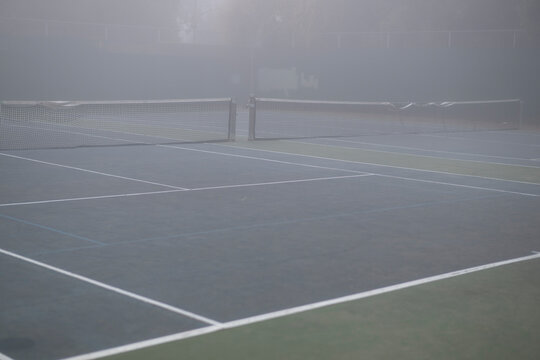 tennis court with damaged nets in dense grey fog