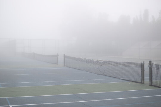 Blue tennis courts with damaged net on thick dense fog