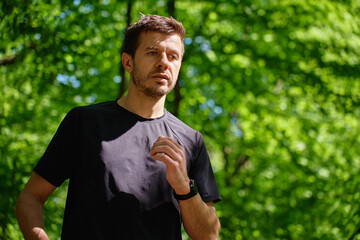 Man running on trail through green park in summer day. Outdoor cardio training in nature. Male...