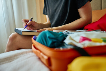 Person writes in notebook with packed orange suitcase full of clothes. Travel concept with...