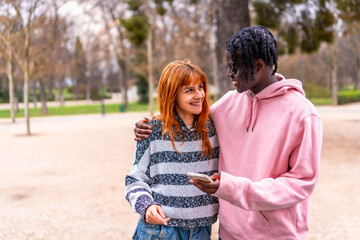 Obraz premium Young couple smiling and using smartphone in park