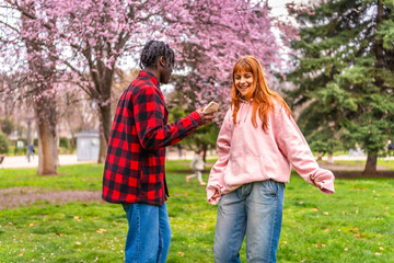 Fototapeta premium Young man filming dancing woman with smartphone in spring park