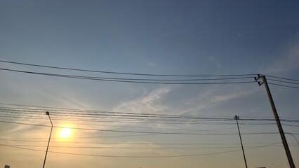 Serene Sky with Wispy Clouds and Power Lines Under a Setting Sun at Dusk in Tranquil Atmosphere