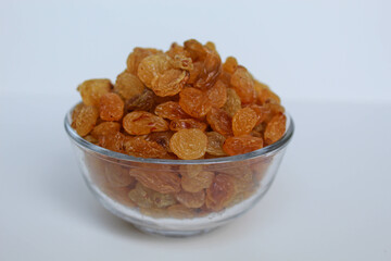 Yellow raisins in a transparent bowl, isolated on white background