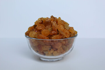Yellow raisins in a transparent bowl, isolated on white background