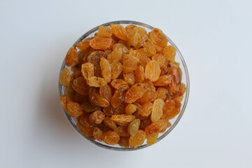 Yellow raisins in a transparent bowl, isolated on white background, flat lay or top view