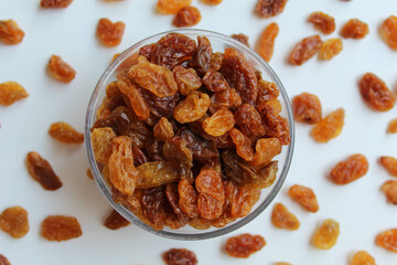 Scattered raisins around transparent bowl, isolated white background, flat lay or top view