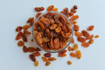 Scattered raisins around transparent bowl, isolated white background, flat lay or top view