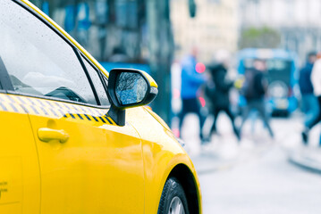 Detail of yellow taxi car against defocused people crossing the street