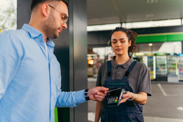 Gas station worker holding a pos terminal while assisting a customer making a payment with a...