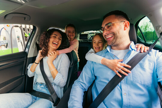 Cheerful family traveling in a modern electric car, enjoying laughter and fun during their road trip. Daughters wearing seatbelts, creating joyful memories together
