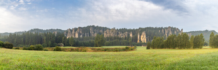 Landscape of Adrspach-Teplice Rocks area, in Hradec Kralove Region in Czech Republic, Europe. Scenic panorama of rock formations, lush forests, and a meadow under a cloudy sky, early morning light.