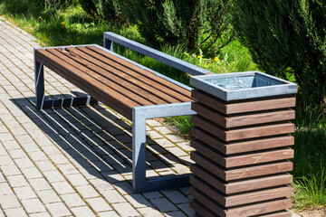 A beautifully crafted wooden bench that has a trash can beside it