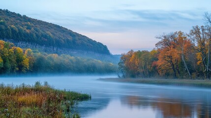 Tranquil autumnal river winding through forested hills in misty morning light.