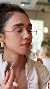 A young woman tries on clear dental aligners at a trendy cafe. She smiles while adjusting the aligners, showcasing her stylish look in a vibrant setting.