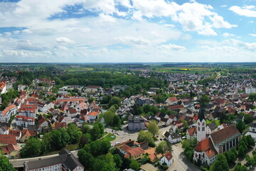Obraz premium Eine beeindruckende Luftaufnahme von Günzburg, einer charmanten Stadt in Bayern. Die Stadt ist geprägt von einer harmonischen Mischung aus historischen und modernen Gebäuden mit roten Ziegeldächern.