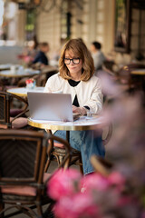 Obraz premium Mid aged businesswoman sitting at outdoor cafe and working on her laptop