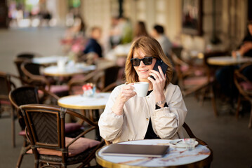 Mid aged businesswoman sitting at outdoor cafe and and talking to someone on the phone