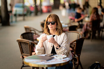 Mid aged businesswoman sitting at outdoor cafe and drinking coffee