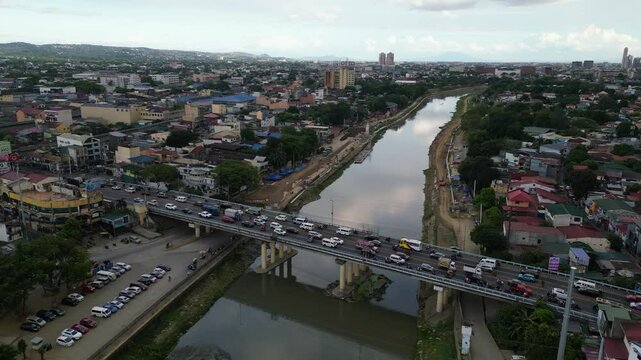 Medium drone approach to bridge crossing Marikina River cutting through dense urban area in Metro Manila at daylight, evening traffic commute