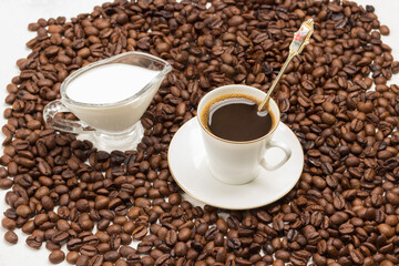 Cup of coffee and cream among roasted coffee beans.