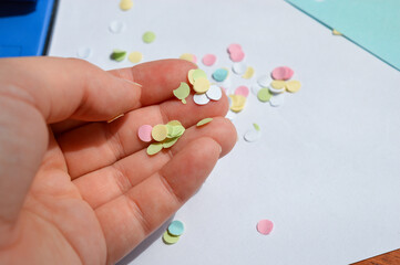 A hand using a blue paper hole puncher on a stack of colored sticky notes. Office and stationery concept with close-up focus.