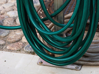 A thick green water hose is wrapped around a stand, Flexible garden hosepipe coiled on metal holder