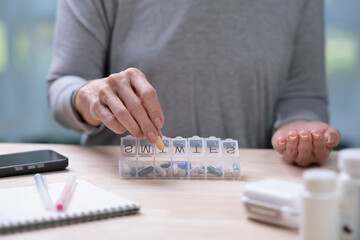 A middle-aged woman holds pills, taken from a daily pill box.