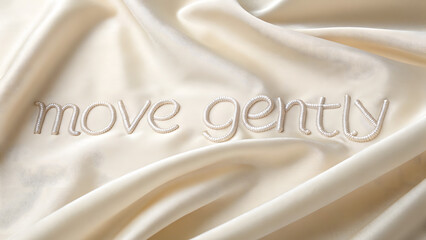 Elegant phrase “Move Gently” written with delicate silk threads on smooth cream fabric, symbolizing softness, mindfulness, and graceful intentional living