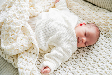 Closeup of cute newborn baby boy in light clothes at home. Eco Baby bed. Home.