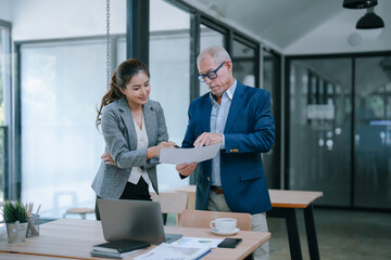 Senior manager and young businesswoman reviewing and discussing a document together in modern office, working together on a project, sharing ideas and expertise