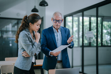 Senior manager holding documents explaining marketing strategy to young businesswoman standing next...