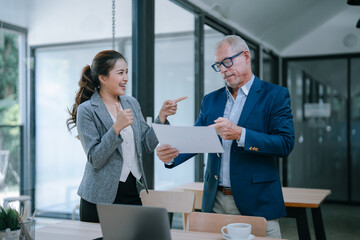 Senior businessman pointing at document and discussing with young businesswoman showing thumbs up, happy with good deal, partnership, and success in business