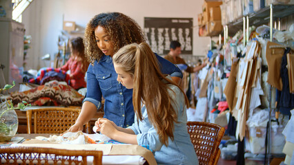 Two Young Women Working In Fashion Design Studio Meeting And Discussing Fabric Samples