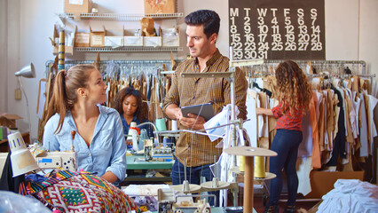 Male Supervisor With Digital Tablet Talking To Woman Using Sewing Machine In Clothing Factory