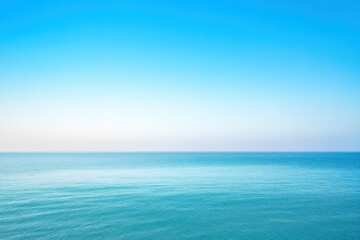 Obraz premium Vast expanse of a clear blue sky meeting a serene turquoise ocean. A horizon line divides the image, with a pale, diffused light suggesting a sunrise or sunset